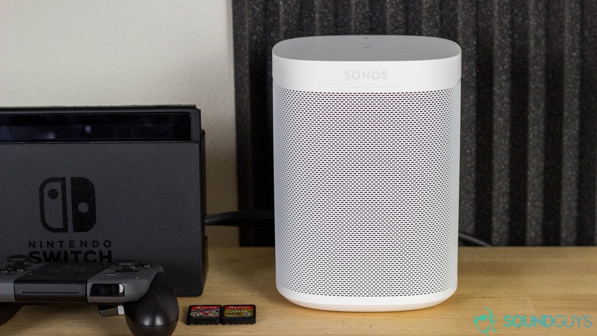 Sonos One Alexa扬声器旁边的Nintendo Switch旁边的木质桌子上，背景带有声泡沫。
