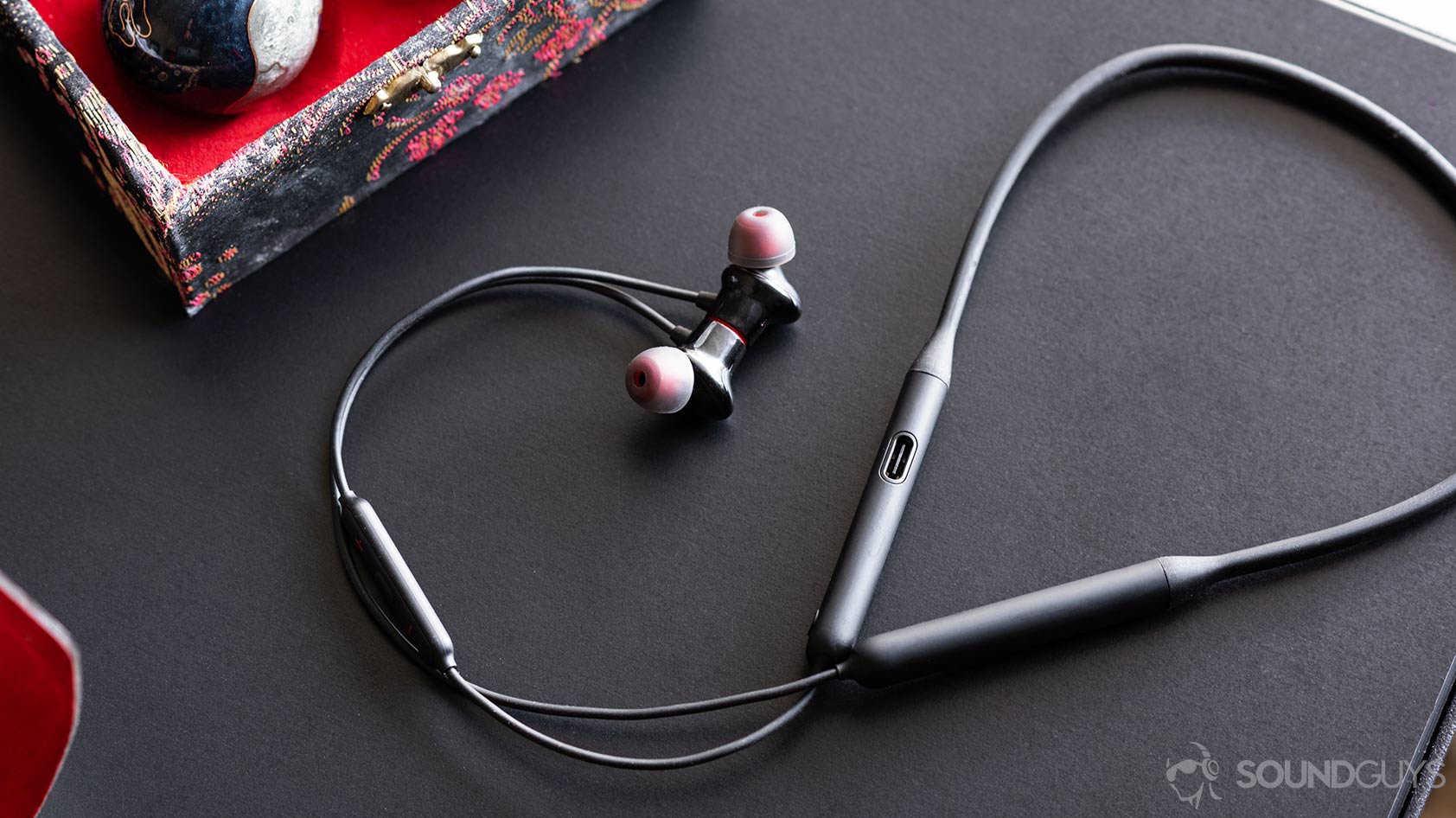 OnePlus子弹无线的图片2耳塞和颈带，电缆在黑色桌子上弯曲。