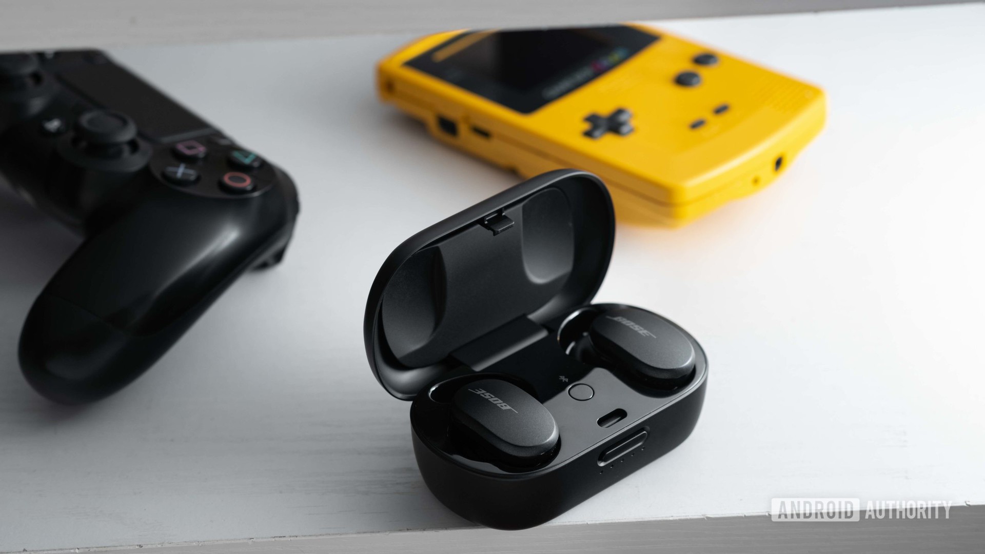 Bose Quietcomfort耳塞在USB-C充电箱中降噪，在GameBoy Color和PlayStation 4控制器旁边。