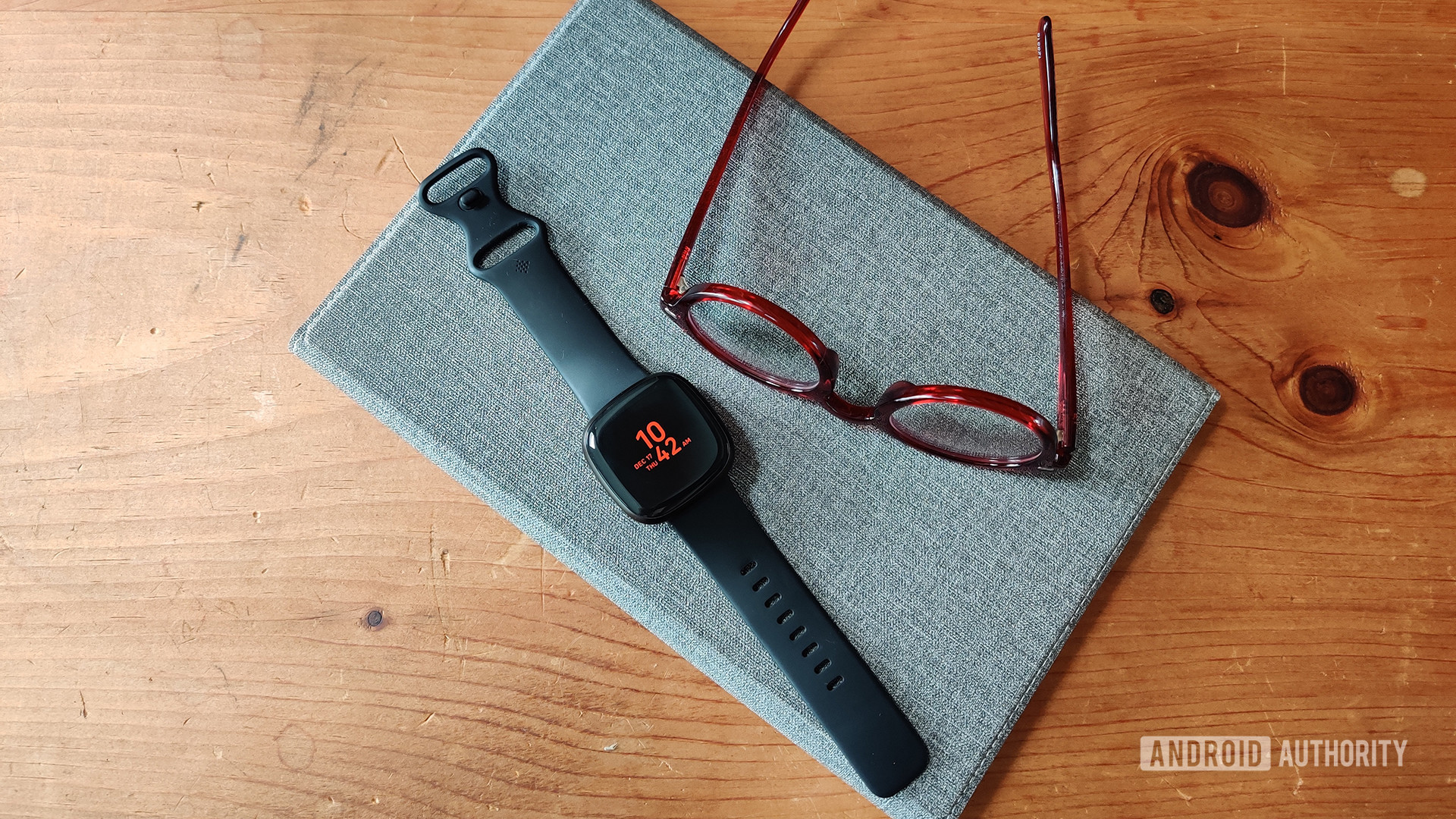 最好的Fitbit智能手表，即Versa 3，沿着一双阅读眼镜放在旁边。
