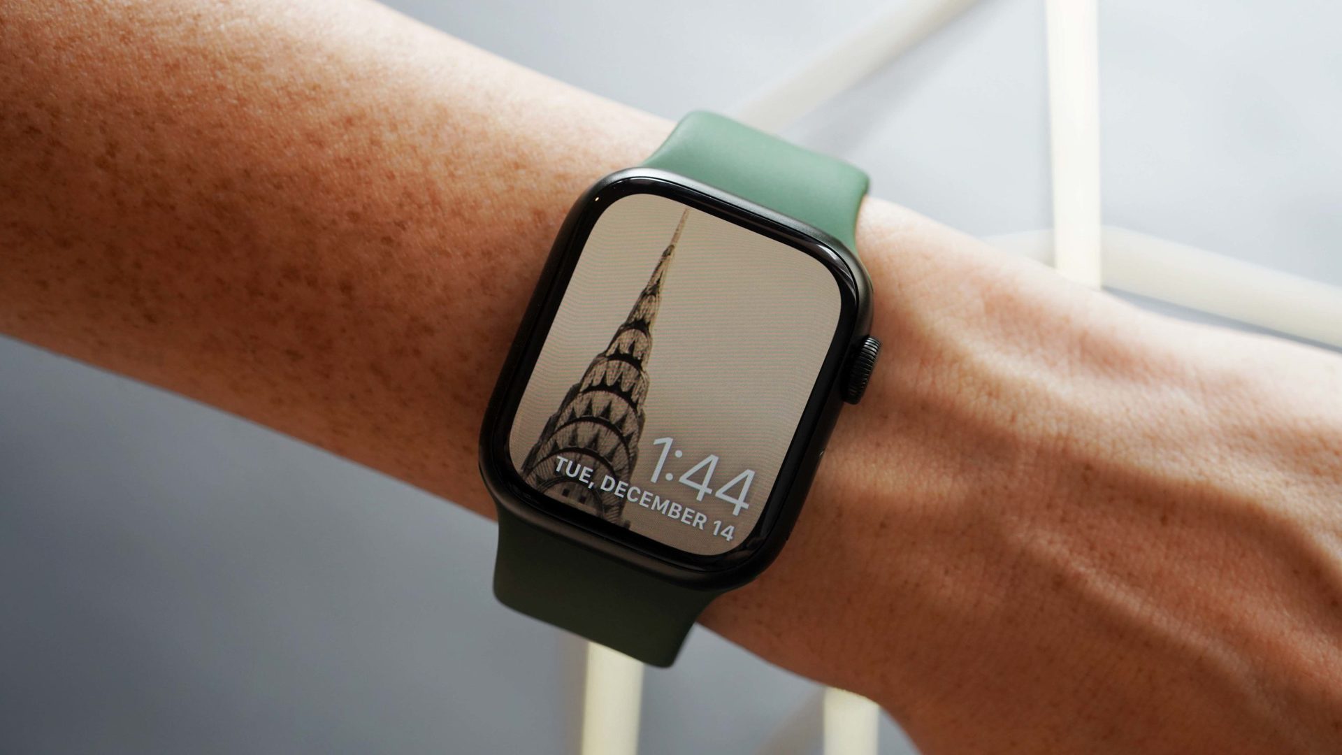 用户手腕上的Apple Watch系列7显示了他们的照片表面上的Chrysler建筑物的图像。