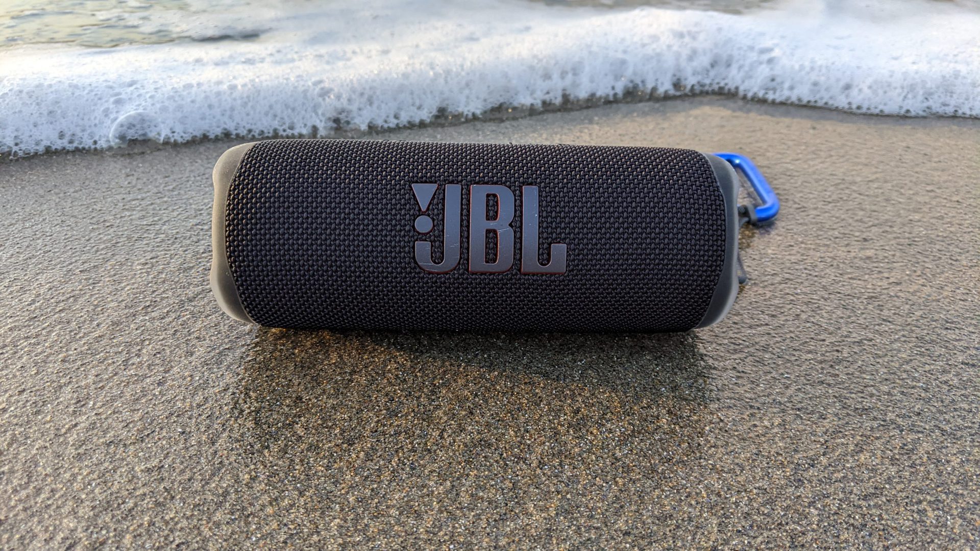 JBL翻转6个蓝牙扬声器坐在海洋的湿沙上。